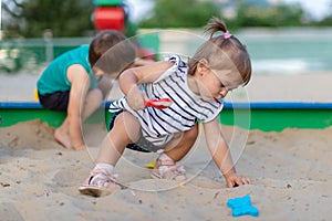 Cute toddler girl playing in sand on outdoor playground. Beautiful baby in red trousers having fun on sunny warm summer day. Child