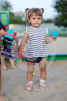 Cute toddler girl playing in sand on outdoor playground. Beautiful baby in red trousers having fun on sunny warm summer day. Child