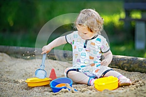 Cute toddler girl playing in sand on outdoor playground. Beautiful baby in summer clothes having fun on sunny warm