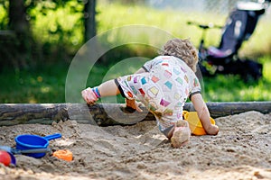 Cute toddler girl playing in sand on outdoor playground. Beautiful baby in summer clothes having fun on sunny warm