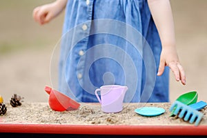 Cute toddler girl playing in a sandbox with moulds and pinecones