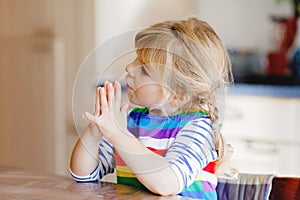 Cute toddler girl praying to God at home. Child using hands for pray and thank for food. Christian tradition.