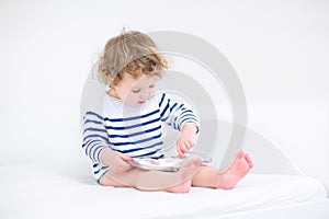 Cute toddler girl reading a book in white bedroom