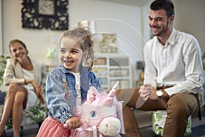 Cute toddler girl riding a pink unicorn rocking horse in a furniture shop, lovely family in a home decor shop together