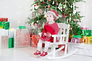 Cute toddler girl in santa hat sitting under Christmas tree