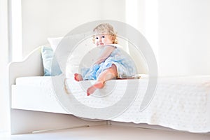 Cute toddler girl sitting on a white bed at home