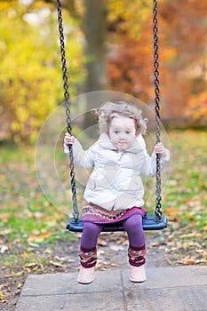 Cute toddler girl on swing with autumn trees