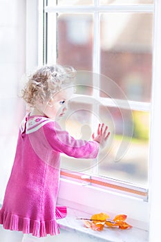 Cute toddler girl watching out of a window