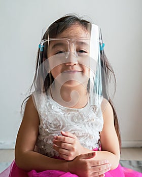 A cute toddler girl wearing the face protection shield. A safety face shield corona mask during Covid-19 pandemic