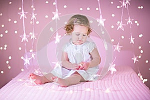 Cute toddler girl in a white bed between pink lights