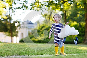 Cute toddler girl in yellow rubber boots and toy with rain drops