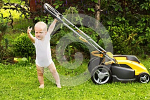 Cute toddler with a lawnmower cutting grass