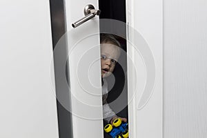 Cute toddler looking out from behind the ajar door