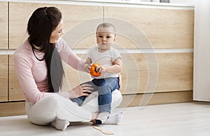Cute toddler playing with fresh pepperbell, sitting with mom on kitchen floor