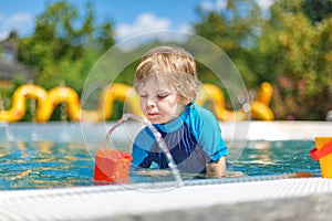 Cute toddler playing with water by the outdoor swimming pool