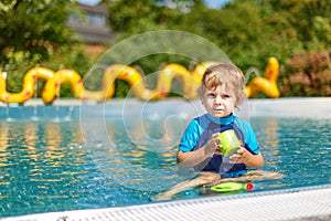 Cute toddler playing with water by the outdoor swimming pool