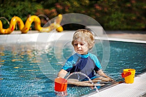 Cute toddler playing with water by the outdoor swimming pool