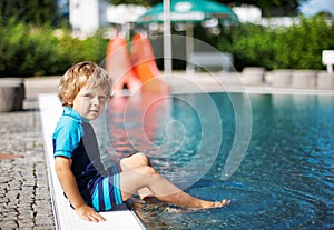 Cute toddler playing with water by the outdoor swimming pool