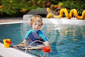 Cute toddler playing with water by the outdoor swimming pool