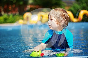 Cute toddler playing with water by the outdoor swimming pool