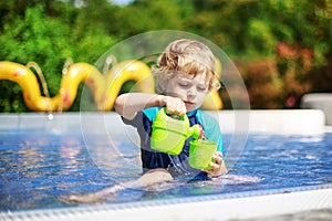 Cute toddler playing with water by the outdoor swimming pool