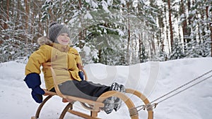 cute toddler is riding sledge in winter forest, having fun and joy during family walk in nature