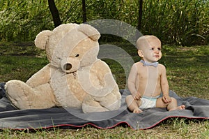 Cute toddler with teddy bear sitting on the ground with diaper