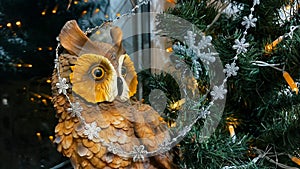 Cute toy owl near Christmas tree with garland in shape of silver snowflakes against golden bokeh lights reflecting in