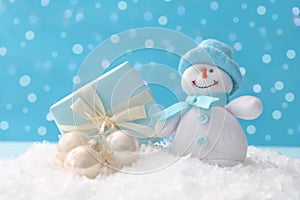 Cute toy snowman, gift box and Christmas balls on snow against blurred background