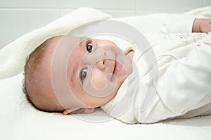 Cute tree months old baby boy dressed in white body looking at the camera while laying on the baby changer