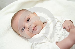 Cute tree months old baby boy dressed in white body looking at the camera while laying on the baby changer