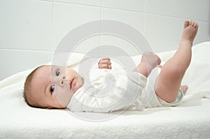 Cute tree months old baby boy dressed in white body looking at the camera while laying on the baby changer