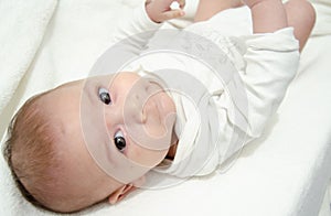 Cute tree months old baby boy dressed in white body looking at the camera while laying on the baby changer