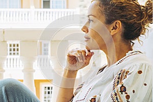 Cute trendy woman sitting outside home in the terrace having relax time looking in front. Side portrait of young adult female