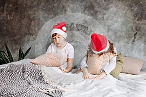 Cute tween children in Santa hats don`t want to wake up on bed with pillow in loft bedroom, christmas morning time