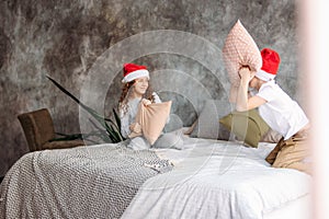 Cute tween children in Santa hats and pajamas playing on bed with pillow, christmas morning time, kids party