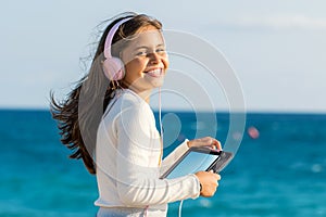 Cute tween girl with headphones and tablet outdoors