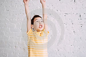 Cute tween happy win boy with funny face in yellow t-shirt isolated on white brick wall background