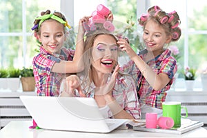 Cute tweenie girls and mother in hair curlers with laptop at home