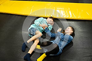 Cute twin brother and sister jumping and bouncing on indoor trampoline together when spending time in children play center. Sports