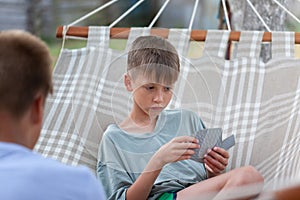 Cute two boys brothers are sitting in hammock an summer day and playing cards outdoors