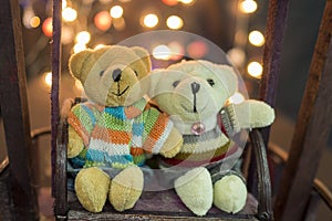 Cute two doll bears. Pair of cute teddies are sitting on wood swing with bokeh light in background. Teddies wear winter suite. Hug