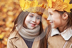 Cute two little sisters with crown of leaves hugging in autumn park