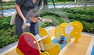 A little boy is playing on a swing with his mom