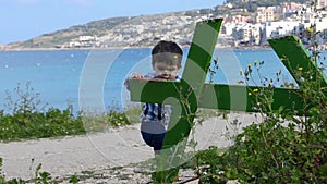 Cute two years old baby boy climbing on green broken table in the park sea in the background