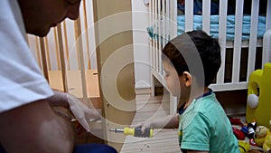 Cute two years old boy helping his father to lover down cot for his baby brother