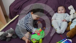 Cute two years old boy playing with turtle education toy while his baby brother is watching and smiling
