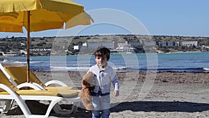 Cute two years old boy with teedy bear on the sandy beach colder weather