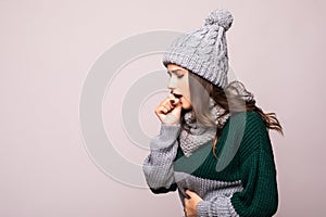 Cute unhealthy female in hat, wrapped in warm scarf sneezing, experiences allergy symptoms, caught a cold. Sick desperate woman