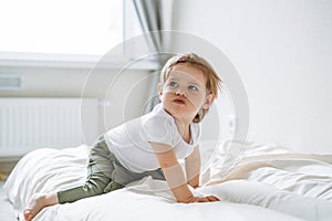 Cute upset baby girl angry child in home clothes sitting on bed at home